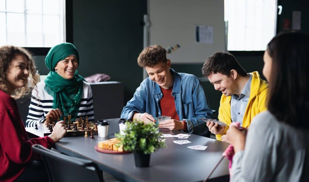 Group of people playing cards and board games in community center, inclusivity of disabled person